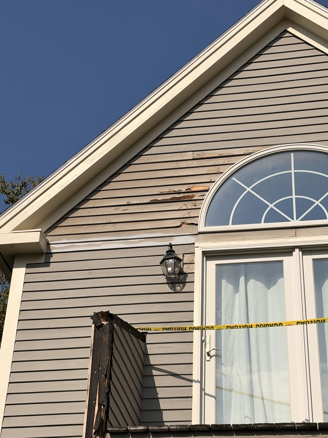 Peeling siding around an arched window before repair and paint