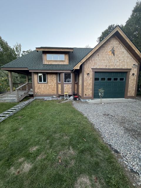 Cedar shingle home with dark green roof and garage door